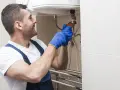 Instalator w niebieskich rękawiczkach dokręca zawór, pokazując, jak spuścić wodę z bojlera.