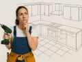 Kobieta w ogrodniczkach z wiertarką zastanawia się nad projektem kuchni.