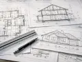 Plany architektoniczne domu, przekroje i rzuty. Linijka i długopis leżą na rysunkach, które określają nieprzekraczalna linia zabudowy.