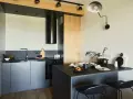 Nowoczesna kuchnia z wyspą i czarnym okapem. Drewniane elementy i minimalistyczne dekoracje. Idealne rozwiązanie, jak oddzielić kuchnię od salonu.