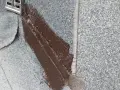 Fragment dachu pokryty papą z posypką, gdzie świeżo nałożona brązowa masa bitumiczna uszczelnia połączenie z metalowym elementem.