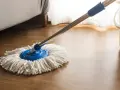 Mop z białymi sznurkami na drewnianej podłodze, obok wiaderka. Idealny do pytania: czym myć panele.