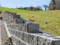 Budowa taniego murku oporowego z bloczków betonowych. Widać drabinę i różową nić traserską.