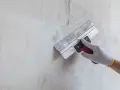 Ręka w rękawicy nakłada gładź na ścianę za pomocą kielni.