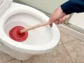 Ręka z przepychaczem w toalecie. Prosty sposób, jak odetkać kibel, gdy woda stoi.