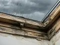 Zniszczone drewniane okno dachowe z pleśnią i zaciekami na ścianie.
