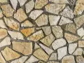 Chropowata ściana z nieregularnych, żółtawych i białych kamieni piaskowca, połączonych szarą zaprawą.