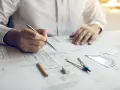 Inżynier z uprawnieniami budowlanymi elektrycznymi analizuje projekt, trzymając długopis nad dokumentacją techniczną.
