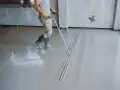 Robotnik wyrównuje świeżą wylewkę betonową. Sprawdź, jaka jest cena wylewki betonowej i jak przebiega jej wykonanie.