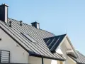 Nowy dom z czarnym, metalowym dachem i kominem. Widać świetlik dachowy, który doświetla wnętrze.