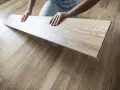 Układanie paneli w kuchni. Dłonie trzymają jasny panel laminowany, który ma imitować drewno.