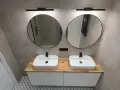Nowoczesna wizualizacja łazienki z dwoma umywalkami, okrągłymi lustrami i drewnianym blatem.