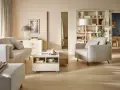 Jasny salon z sofą, fotelem i stolikiem kawowym na kółkach. Na półkach regału stoją dekoracje, książki i lampa. Wersaliki dodają elegancji.