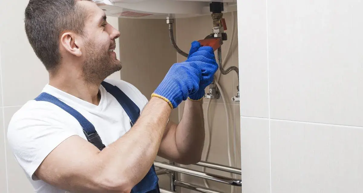 Instalator w niebieskich rękawiczkach dokręca zawór, pokazując, jak spuścić wodę z bojlera.