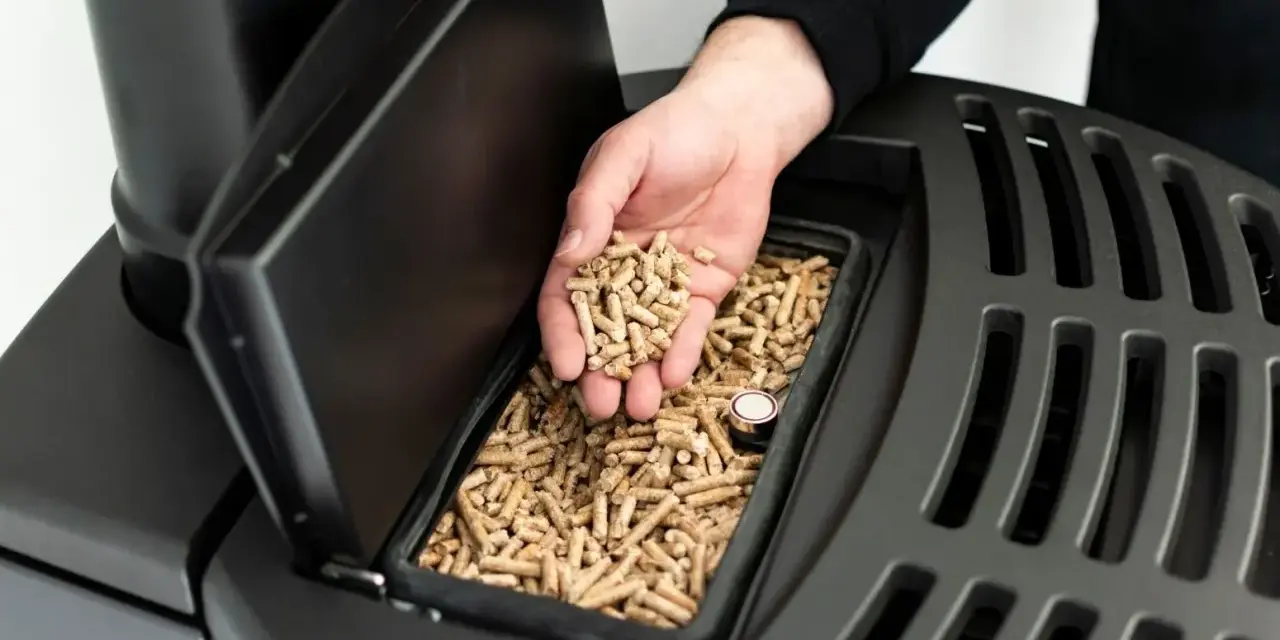 Dłoń wsypuje pellet do zasobnika pieca na pellet i drewno. Opinie o tym modelu są pozytywne.