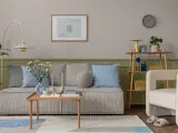Przytulny salon z kanapą w paski, poduszkami w odcieniach błękitu i zieleni, stolikiem kawowym i fotelem. Ściany w kolorze szałwiowym tworzą spokojną atmosferę.