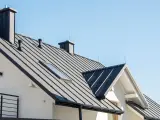 Nowy dom z czarnym, metalowym dachem i kominem. Widać świetlik dachowy, który doświetla wnętrze.