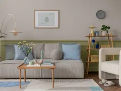 Przytulny salon z kanapą w paski, poduszkami w odcieniach błękitu i zieleni, stolikiem kawowym i fotelem. Ściany w kolorze szałwiowym tworzą spokojną atmosferę.
