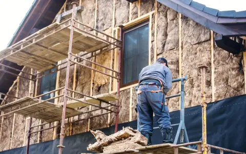 Budowa domu: pracownik na rusztowaniu izoluje ścianę.