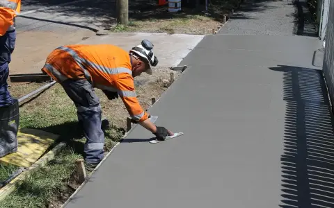 Robotnik w pomarańczowej kamizelce wygładza świeży beton kielnią.