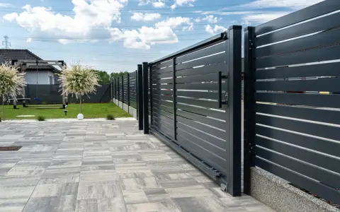 Solidny fundament pod bramę przesuwną zapewnia jej stabilność i płynne działanie. Nowoczesna, ciemnoszara brama z poziomymi lamelami.