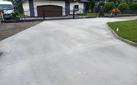 Nowy podjazd z betonu przed domem z garażem i bramą.