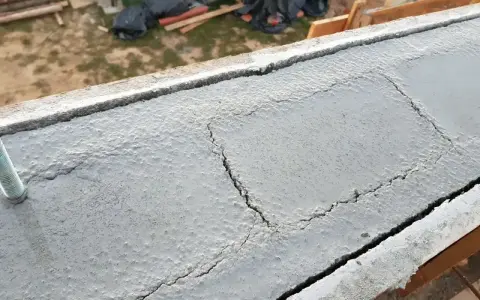Betonowy wieniec budowlany z widocznymi pęknięciami i wystającym prętem.
