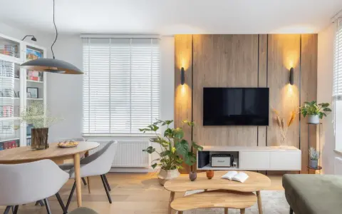 Przytulny salon inspiracje: drewniana ściana z TV, okrągły stół z krzesłami, rośliny i stylowe oświetlenie tworzą ciepłą atmosferę.
