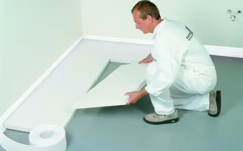 Mężczyzna w białym kombinezonie układa styropian na podłodze.