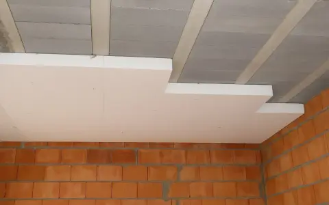 Białe płyty styropianowe montowane do betonowego stropu, przygotowanie do tynkowania sufitu. Widoczne ceglane ściany.