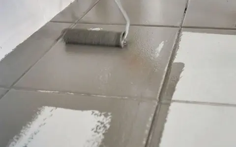 Malowanie płytek podłogowych wałkiem, nadawanie im nowego, szarego koloru.
