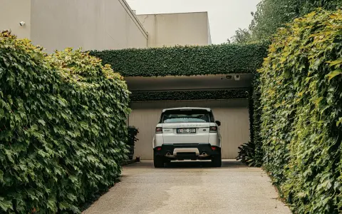 Biały Range Rover wjeżdża na podjazd otoczony bujną zielenią. Naturalna ściana z bluszczu to świetna alternatywa co zamiast kostki na podjazd.