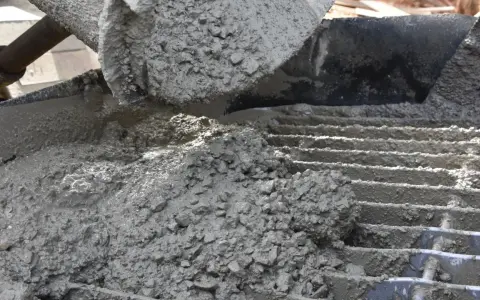 Świeży beton z kruszywem, idealny jako jaki beton pod obrzeża, wylewany z maszyny na ruszt.