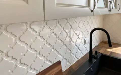 Białe, wypukłe płytki w kształcie arabeski tworzą elegancką mozaikę nad blatem kuchennym.