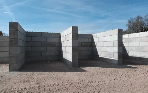 Budowa muru oporowego z betonowych bloczków na piaszczystym podłożu.