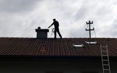 Kominiarz na dachu sprawdza komin. Zastanawiasz się, ile kosztuje przegląd kominiarski?