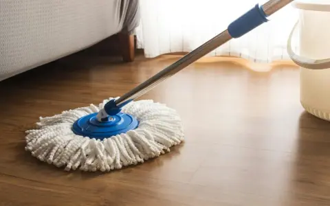 Mop z białymi sznurkami na drewnianej podłodze, obok wiaderka. Idealny do pytania: czym myć panele.