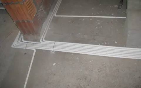 Uporządkowana instalacja elektryczna w podłodze, biegnąca wzdłuż ściany z cegły.