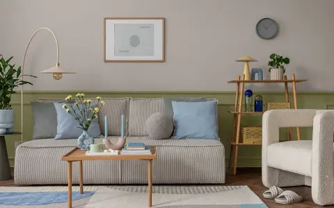 Przytulny salon z kanapą w paski, poduszkami w odcieniach błękitu i zieleni, stolikiem kawowym i fotelem. Ściany w kolorze szałwiowym tworzą spokojną atmosferę.
