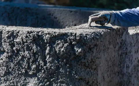 Dłoń w rękawicy wygładza mokry beton na budowie.