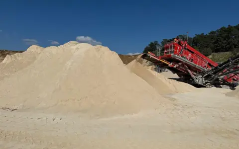 Góra piasku, prawdopodobnie wapno węglanowe, obok czerwonej maszyny do przesiewania na placu budowy.