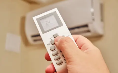 Dłoń trzymająca pilot do klimatyzatora, ustawiająca temperaturę 24°C. Ogrzewanie klimatyzatorem zapewnia komfort.