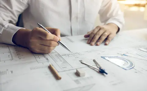 Inżynier z uprawnieniami budowlanymi elektrycznymi analizuje projekt, trzymając długopis nad dokumentacją techniczną.