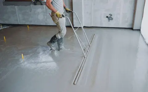 Robotnik wyrównuje świeżą wylewkę betonową. Sprawdź, jaka jest cena wylewki betonowej i jak przebiega jej wykonanie.