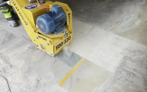 Żółta maszyna do szlifowania betonu RM-320 pracuje na posadzce, tworząc pył.