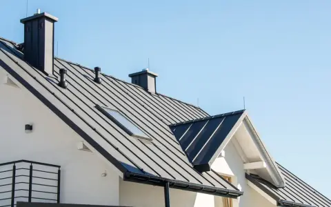 Nowy dom z czarnym, metalowym dachem i kominem. Widać świetlik dachowy, który doświetla wnętrze.