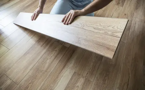 Układanie paneli w kuchni. Dłonie trzymają jasny panel laminowany, który ma imitować drewno.