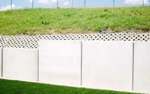 Betonowy mur oporowy z ażurową warstwą i zieloną skarpą.