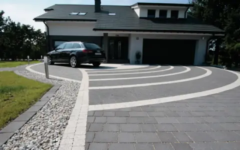 Nowoczesny dom z garażem, przed którym rozciąga się efektowny beton na podjazd, ozdobiony białymi pasami tworzącymi łuki.