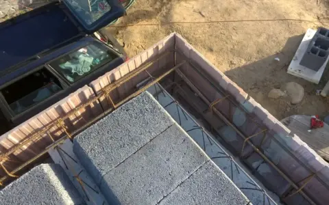 Budowa stropu ackermana w toku. Betonowe pustaki i zbrojenie czekają na zalanie betonem. Obok stoi samochód.